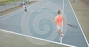 Two diverse male friends playing doubles returning ball on outdoor tennis court in slow motion