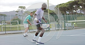 Two diverse male friends playing doubles returning ball on outdoor tennis court in slow motion