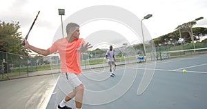 Two diverse male friends playing doubles returning ball on outdoor tennis court in slow motion