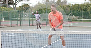 Two diverse male friends playing doubles returning ball over net at outdoor court in slow motion