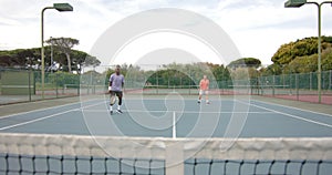 Two diverse male friends playing doubles returning ball over net at outdoor court in slow motion