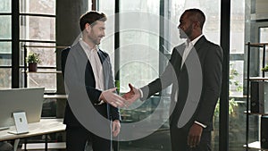 Two diverse men multiracial businessmen talking in office shake hands after successful negotiations. Caucasian man