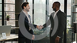 Two diverse men multiracial businessmen talking in office shake hands after successful negotiations. Caucasian man