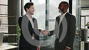 Two diverse multiracial businessmen business colleagues partners men handshaking in office posing smiling to camera
