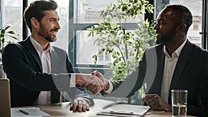 Two diverse multiracial businessmen signing document agreement shaking hands success business deal. Multiethnic men