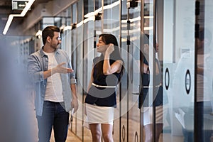 Two diverse professional coworkers talking walking in office corridor