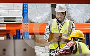 Two diverse professional male workers holding board, checking shipping stocks in storage, warehouse or factory for delivery,