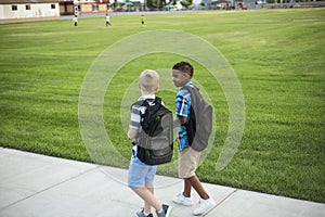 Two diverse school kids walking and talking together on the way to school