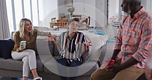 Two diverse senior couples sitting on a couch drinking tea together at home