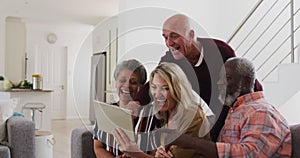 Two diverse senior couples sitting on a couch using a digital tablet and laughing