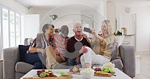 Two diverse senior couples sitting on a couch using a smartphone and laughing