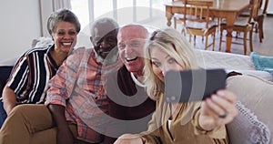 Two diverse senior couples sitting on a couch using a smartphone and taking a selfie