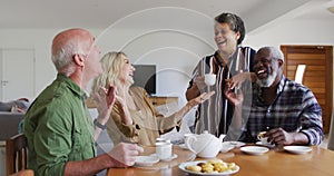 Two diverse senior couples sitting by a table drinking tea together at home