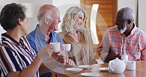 Two diverse senior couples sitting by a table drinking tea together at home