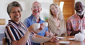 Two diverse senior couples sitting by table drinking tea together at home