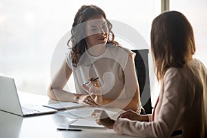 Two diverse serious businesswomen talking working together in office