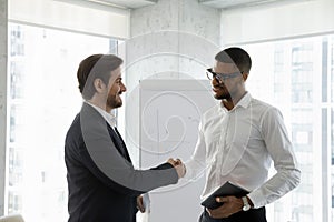 Two diverse smiling business men shaking hands in office boardroom