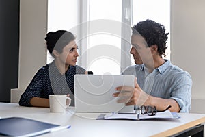 Two diverse team coworkers sharing computer at workplace