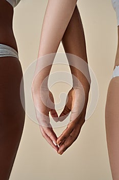 Two diverse women wearing underwear touching hands making heart, vertical.