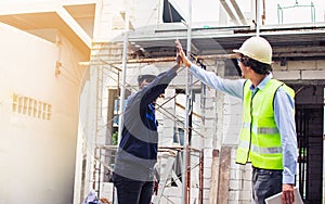 Two diversity male engineers team working, inspecting outdoor at construction site, wearing hard hats for safety, giving high five