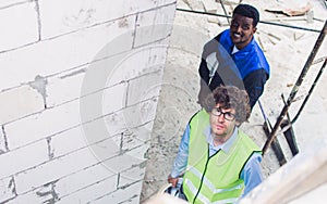 Two diversity male engineers team working, inspecting outdoor at construction site, wearing hard hats for safety, looking at