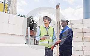 Two diversity male engineers team working, inspecting outdoor at construction site, wearing hard hats for safety, talking,