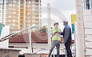 Two diversity male engineers team working, inspecting outdoor at construction site, wearing hard hats for safety, talking,