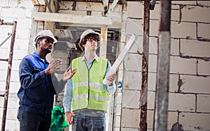 Two diversity male engineers team working, inspecting outdoor at construction site, wearing hard hats for safety, talking,