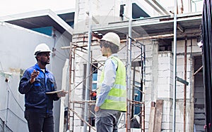 Two diversity male engineers team working, inspecting outdoor at construction site, wearing hard hats for safety, talking,