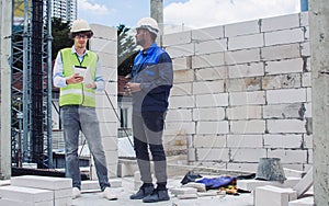 Two diversity male engineers team working, inspecting outdoor at construction site, wearing hard hats for safety, talking,