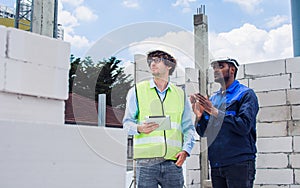 Two diversity male engineers team working, inspecting outdoor at construction site, wearing hard hats for safety, talking,