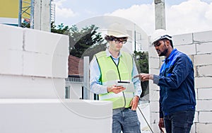 Two diversity male engineers team working, inspecting outdoor at construction site, wearing hard hats for safety, talking,