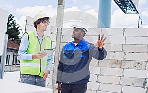 Two diversity male engineers team working, inspecting outdoor at construction site, wearing hard hats for safety, talking,