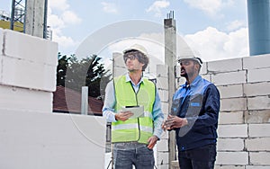 Two diversity male engineers team working, inspecting outdoor at construction site, wearing hard hats for safety, talking,