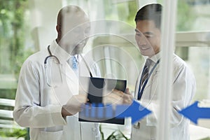 Two doctors consulting over medical record on the other side of glass doors