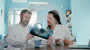 Two doctors dentist are examining x-ray photograph using loupe and laptop