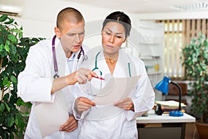 Two doctors discussing medical card of patient in office