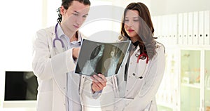 Two doctors examine x-ray of a broken leg. Doctor points to the x-ray and woman surgeon listens attentively