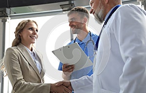 Two doctors and female patient shaking hands before consultation in the office of a modern medical center