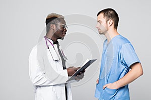 Two doctors meeting and consulting each other on gray background. Caucasian doctor and afroamerican doctor talking abount pacient