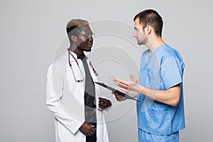 Two doctors meeting and consulting each other on gray background. Caucasian doctor and afroamerican doctor talking abount pacient