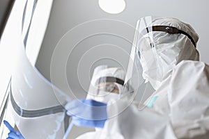 Two doctors in protective screens and anti-plague suit are looking at x-ray in clinic