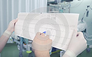 Two doctors reading ECG chart in the intensive care unit next to the patient bed