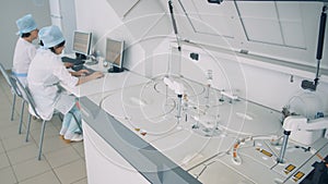 Two doctors sit at computers, while laboratory testing equipment is in process.