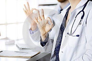 Two doctors sitting with Ok sign in hospital office. Medical help, countering viral infection and medicine concept