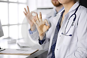 Two doctors sitting with Ok sign in hospital office. Medical help, countering viral infection and medicine concept