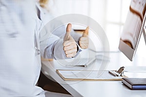 Two doctors sitting with thumbs up in hospital office. Medical help, countering viral infection concept