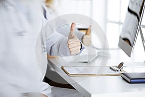 Two doctors sitting with thumbs up in hospital office. Medical help, countering viral infection and medicine concept