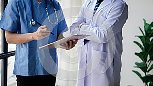 Two doctors stand in a conference room discussing, brainstorming on how to plan a patient's treatment in a complex case that