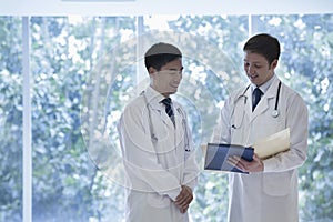 Two doctors standing, looking down, and consulting over medical record in the hospital